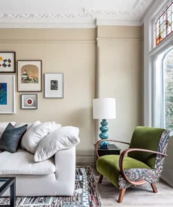 Front room with cream couch, beige painted walls, outlined exhibition wall, dull wood and green well proportioned relax seat, blue and white table light 